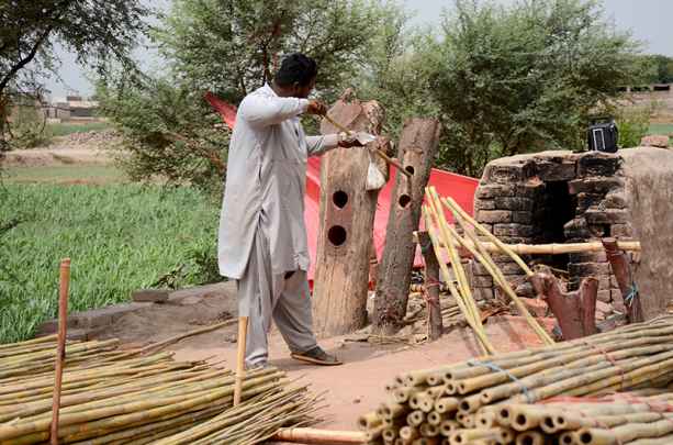 Worker Straightens Raw Bamboo Poles at Workplace